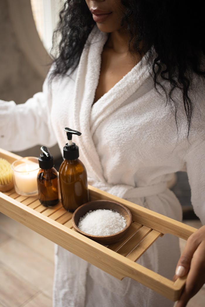 A woman in a bathrobe holds a tray of natural spa products, focusing on self-care.